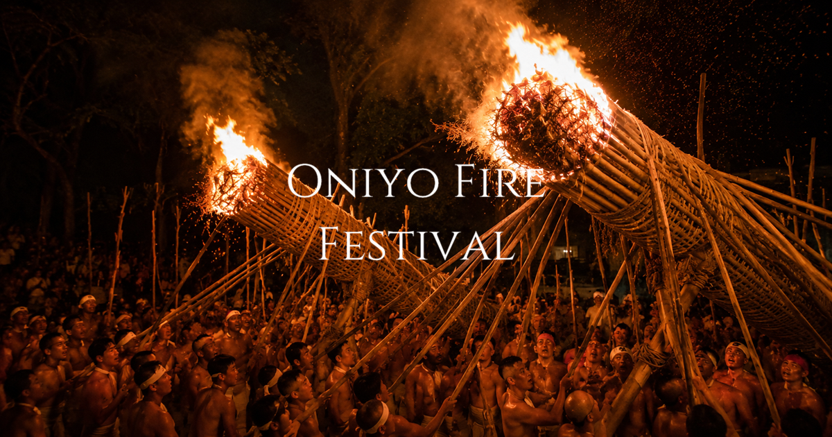 Two large flaming torches are raised above a crowd of participants during a nighttime fire festival.