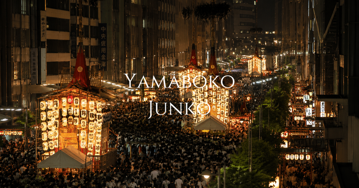 Lantern-lit Yamaboko floats moving through a crowded Kyoto street at night during the Gion Festival procession.
